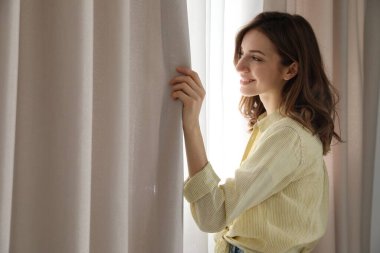 Sabah evde perdeleri açan kadın.