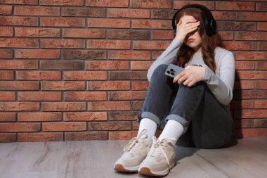 Kulaklıklı üzgün genç kız duvarın içinde müzik dinliyor, mesaj atmak için yer var.