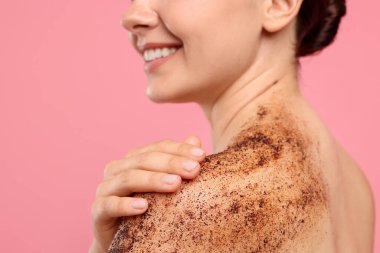 Gülümseyen kadın omuzlarını pembe arka planda ovalıyor, yakın plan.