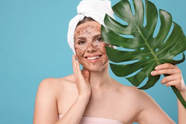 Yüzünde vücut fırçası ve açık mavi arka planda canavar yaprağı olan gülümseyen kadın.