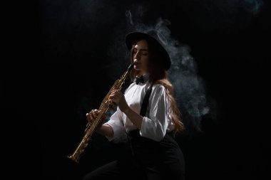 Karanlık arka planda dumanla soprano saksafon çalan müzisyen.