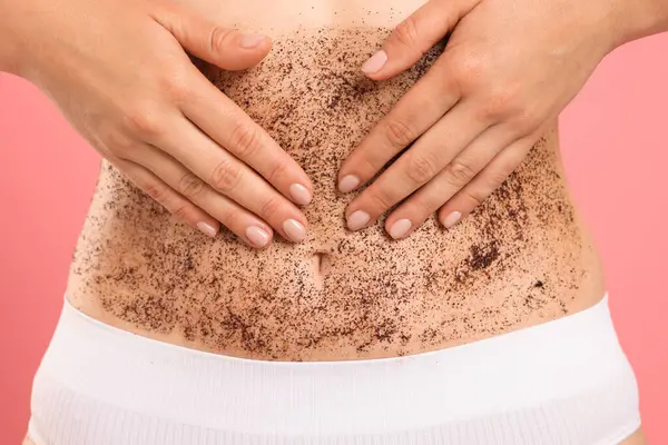 Göbeğini pembe arka plana sürten kadın, yakın plan.