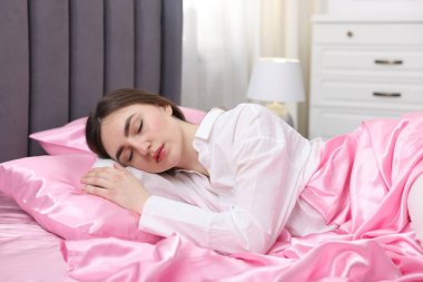 Yatakta pembe ipek çarşaflarla uyuyan bir kadın.