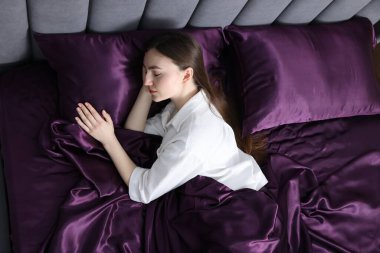 Yatakta mor ipek çarşaflarla uyuyan bir kadın.
