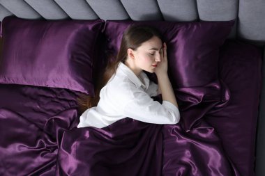 Yatakta mor ipek çarşaflarla uyuyan bir kadın.