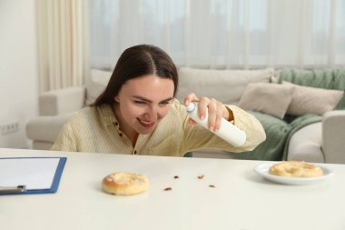 Beyaz masadaki hamamböceklerine böcek ilacı sıkan duygusal genç bir kadın. Haşere sorunu