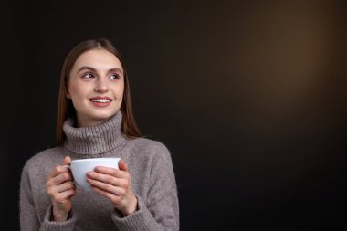 Kahverengi arka planda bir fincan kahveyle gülümseyen kadın. Metin için boşluk