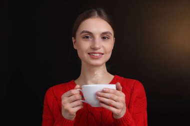 Kahverengi arka planda bir fincan kahveyle gülümseyen kadın.