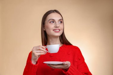 Bej renkli arka planda bir fincan kahveyle gülümseyen kadın