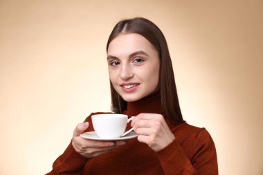 Bej renkli arka planda bir fincan kahveyle gülümseyen kadın