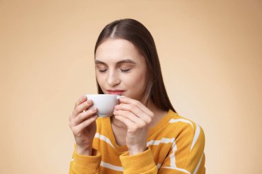 Bej renkli arka planda fincandan kahve içen kadın