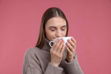 Pembe arka planda bir fincan kahvesi olan kadın.