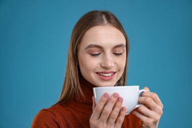 Açık mavi arka planda bir fincan kahveyle gülümseyen kadın.