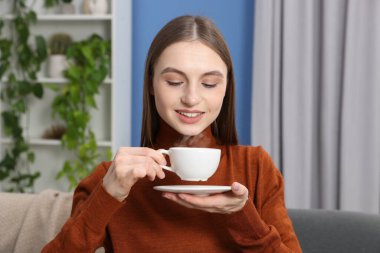 Evdeki kanepede bir fincan kahveyle gülümseyen kadın.