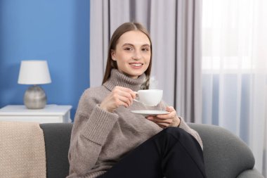 Evdeki kanepede bir fincan kahveyle gülümseyen kadın.