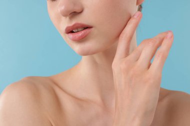 Açık mavi arka planda poz veren güzel kadın, yakın plan.