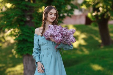 Dışarıda bir demet leylak çiçeğiyle gülümseyen kadın.