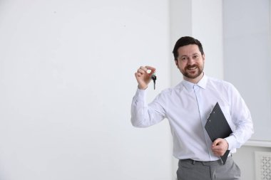 Emlakçının elinde anahtarlık, ev şeklindeki anahtarlık, kapalı alanda pano ve metin için yer var.