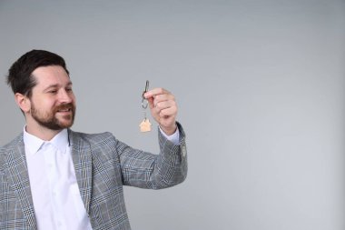 Emlakçının elinde anahtar, ev şekilli anahtarlık açık gri arka planda, metin için boşluk var.