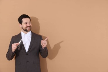 Emlakçının elinde anahtar bej arka planda ev şekilli anahtarlık, metin için boşluk var.