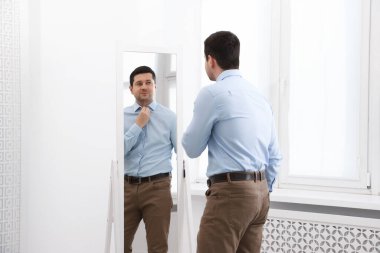 Yakışıklı adam aynada kendine bakıyor.