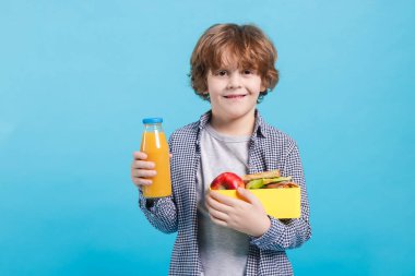 Beslenme çantası olan ve açık mavi arka planda içen sevimli bir çocuk.