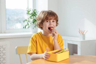 Okuldaki ahşap masada yemek yiyen şirin küçük çocuk.