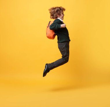 Turuncu arka planda atlayan sırt çantalı tatlı bir okul çocuğu.