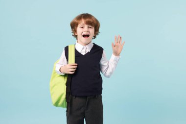 Açık mavi arka planda sırt çantası olan sevimli bir okul çocuğu.