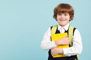 Sırt çantası ve açık mavi arkaplan kitabı olan sevimli bir okul çocuğu.