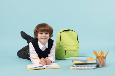 Sırt çantasında açık mavi arka planda çizim yapan sevimli bir okul çocuğu.