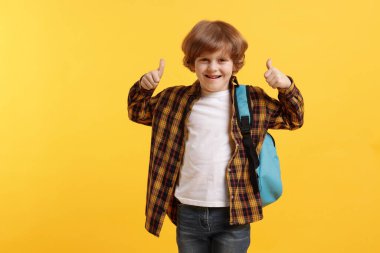 Sırt çantalı yakışıklı okul çocuğu turuncu arka planda baş parmak gösteriyor.
