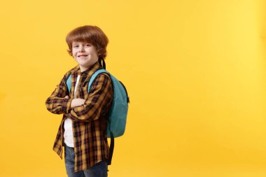 Turuncu arka planda sırt çantası olan tatlı bir okul çocuğu, mesaj için yer var.