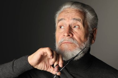 Kıdemli adam gri arka planda makasla sakal buduyor.