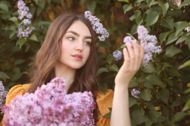 Açık havada çalıların yanında leylak çiçekleri olan güzel bir kadın