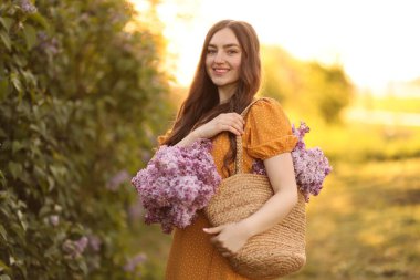 Gülümseyen kadın sabah çalıların yanında bir çanta leylak çiçeğiyle