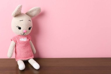 Ahşap masada pembe arka planda sevimli örülmüş oyuncak tavşancık. Metin için boşluk