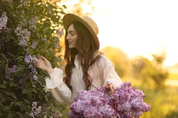 Güzel bir kadın, sabah çalıların yanında bir sepet leylak çiçeği taşıyor.
