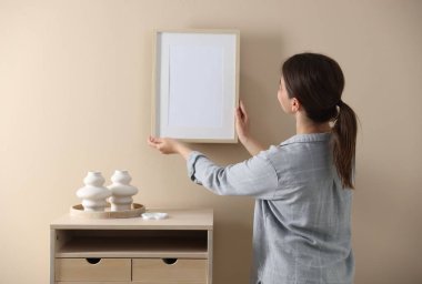 Bej duvarda boş bir çerçeve asılı kadın, arka manzara