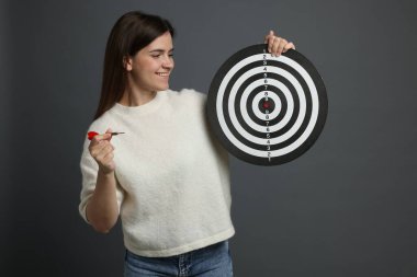 Hedef alınıyor. Gri arka planda ok ve dart tahtası olan gülümseyen kadın.