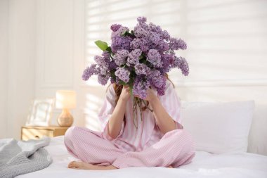 Evdeki yatakta leylak çiçeklerinin arkasına saklanan genç kız.