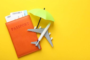 Seyahat sigortası. Uçak modeli, pasaport, küçük şemsiye ve sarı arka planda biletler. Metin için boşluk
