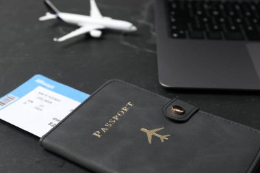 Pasaport, uçuş bileti, uçak modeli ve laptop siyah masada, yakın plan.
