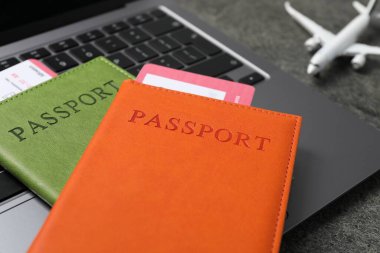 Pasaportlar, uçuş biletleri, uçak modeli ve laptop gri masada, yakın plan.
