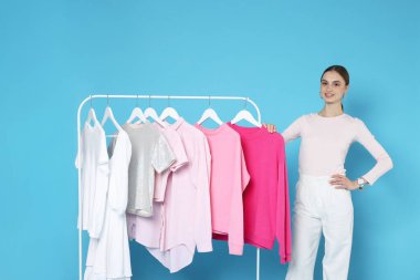 Gülümseyen moda tasarımcısı ve açık mavi arka planda giysileri olan askılar.