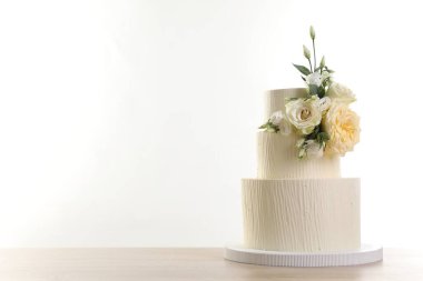 Ahşap masadaki çiçeklerle süslenmiş nefis düğün pastası beyaz arka planda. Metin için boşluk