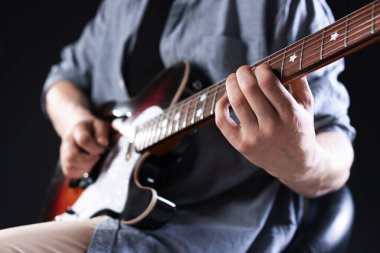 Siyah arka planda gitar çalan adam, ele odaklan.