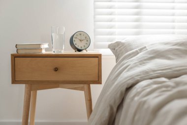 İçinde kitaplar, çalar saat ve yatağın yanında bir bardak su olan komodin.