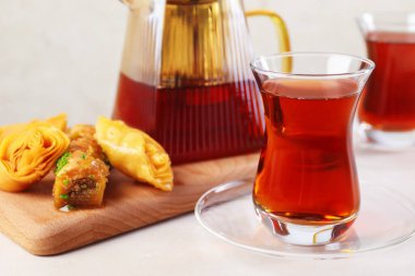 Cam bardaklarda geleneksel Türk çayı, çaydanlık ve beyaz masada taze baklava, yakın plan.