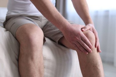 Evdeki yatakta diz ağrısı çeken bir adam, yakın plan.